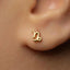 A close-up of a person's ear with a small gold earring featuring a zodiac symbol.