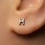 A close-up of a person's ear with a small silver letter 'H' stud earring.
