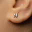 A close-up of a person's ear with a small silver letter 'N' earring.
