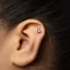 A person's ear with a small silver charm in the shape of a zodiac sign, specifically Capricorn, attached to the earlobe.
