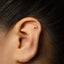 A close-up of a person's ear with a small gold letter H stud earring in the earlobe.