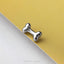 A silver bone-shaped pin is resting on a yellow surface.