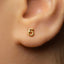 A close-up of a person's ear with a small gold earring featuring the number 6.