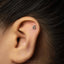 A close-up of a person's ear with a small silver 6-shaped earring inserted in the earlobe.