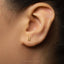 A close-up of a person's ear with a small gold earring featuring the number 8.