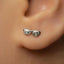 A close-up of a person's ear with a pair of silver earrings featuring a pair of glasses designs.