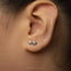 A close-up of a person's ear with a pair of silver earrings featuring a pair of glasses designs.