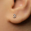 A close-up of a person's ear with a small number 3 earring in it.