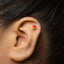 A close-up of a person's ear with a small red earring in the earlobe.