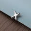 A silver metal object resembling a cross or an X shape is resting on a textured surface, such as a piece of fabric or a piece of paper.