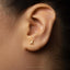 A close-up of a person's ear with a small gold earring featuring a letter 'X' in the center.