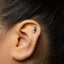 A close-up of a person's ear with a small silver mushroom earring inserted in the earlobe.