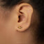 A close-up of a person's ear with a small gold earring in the earlobe.