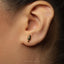 A close-up of a person's ear with a small, gold-colored earring featuring a leaf-like design.