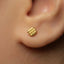 A close-up of a person's ear with a small gold-colored earring in the earlobe.