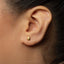 A close-up view of a person's ear with a small gold earring in the earlobe.