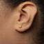 A close-up of a person's ear with a small gold-colored earring in the earlobe.