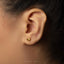 A close-up view of a person's ear with a small gold earring featuring a banana design.