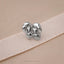 A silver-colored pin or earring is resting on a beige fabric surface.