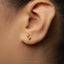 A close-up of a person's ear with a small gold earring featuring a small foot design.