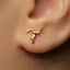 A close-up of a person's ear with a small gold earring featuring a gymnast performing a handstand pose.
