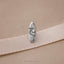 A silver surfboard-shaped pin is resting on a beige fabric surface.