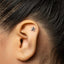 A close-up of a person's ear with a small, silver-colored earring in the earlobe.
