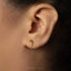 A close-up of a person's ear with a small gold earring in the earlobe.