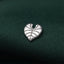 A silver heart-shaped pin is resting on a dark green fabric.