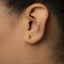 A close-up of a person's ear with a small gold earring in the earlobe.