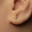 A close-up of a person's ear with a small gold earring featuring a small charm hanging from it.
