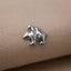 A silver metal pin or badge with a bear-like design on a beige fabric background.