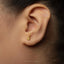 A close-up of a person's ear with a small gold earring featuring a small charm hanging from it.