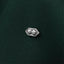 A close-up image of a small silver pin or brooch with two round, reflective surfaces attached to a dark green fabric background.