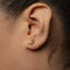 A close-up view of a person's ear adorned with a small gold earring featuring a small bird-like design.