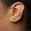 A close-up of a person's ear with a small gold earring in the earlobe.