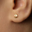 A close-up of a person's ear with a small gold-colored earring featuring a small triangular design.
