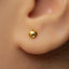 A close-up of a person's ear with a small gold-colored earring inserted.