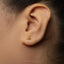 A close-up of a person's ear with a small gold earring featuring an intricate design.