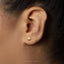 A close-up of a person's ear with a small gold-colored earring featuring a small triangular design.