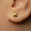 A close-up view of a person's ear wearing a small gold-colored earring with a small television icon on it.