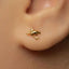 A close-up view of a person's ear adorned with a small gold earring featuring a shark design.