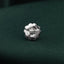 A silver flower-shaped charm is resting on a dark green fabric.