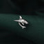 A silver shark pin is resting on a dark green fabric.