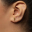 A close-up of a person's ear with a small gold earring featuring an embossed design.