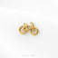 A gold-colored bicycle brooch is displayed against a white background.