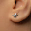 A close-up of a person's ear with a small silver earring featuring a small silver bird or winged design.