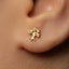 A close-up view of a person's ear with a small gold tree earring in the earlobe.