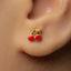 A close-up of a person's ear wearing a small gold earring with a red cherry charm.