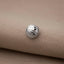 A silver basketball-shaped button is resting on a beige fabric surface.